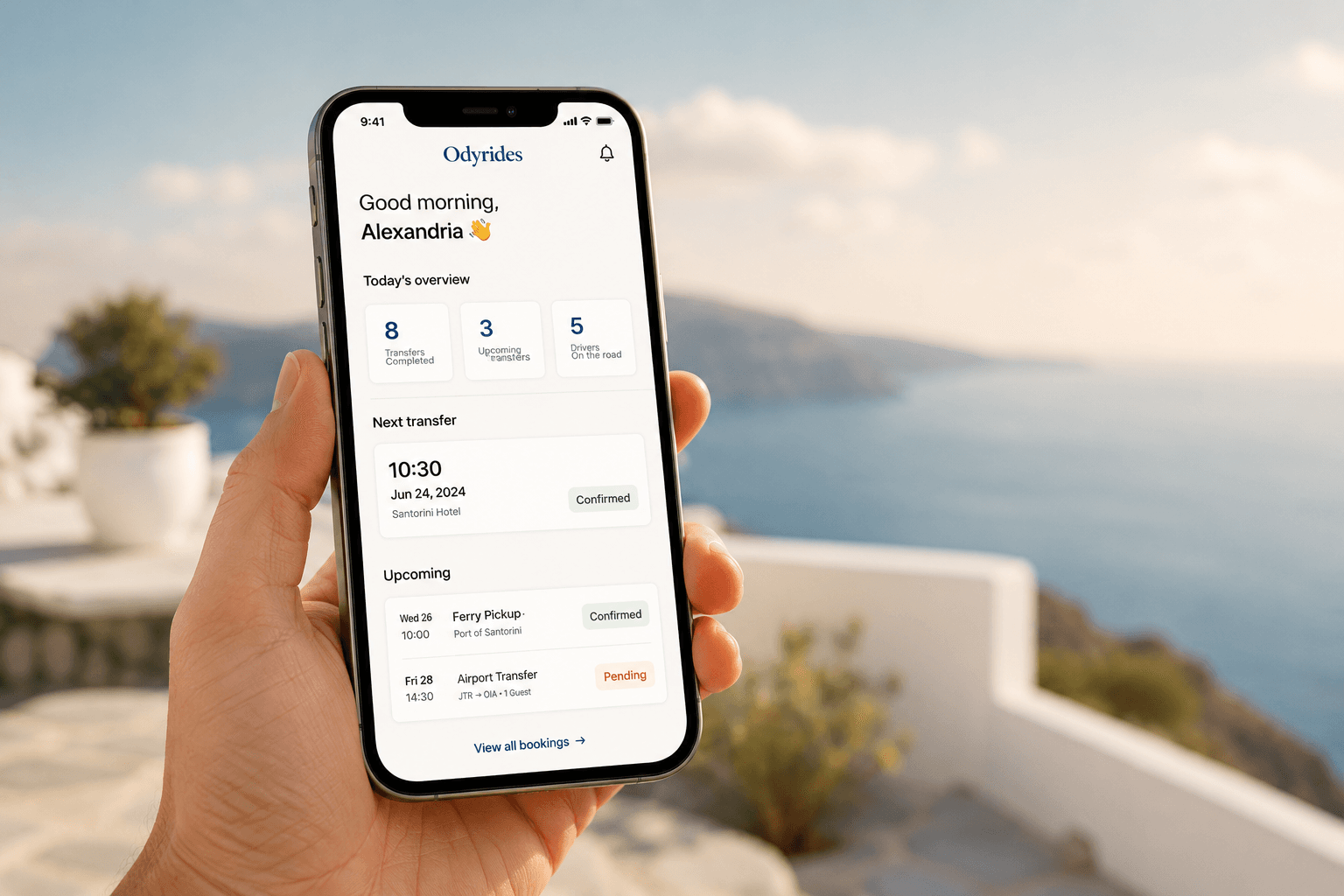 A hand holding a phone showing the Odyrides app on the Greek coast